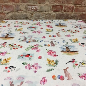 May include: White tablecloth with a repeating pattern of colorful birds, bunnies, flowers, and windmills. The pattern is on a white background with a subtle texture.