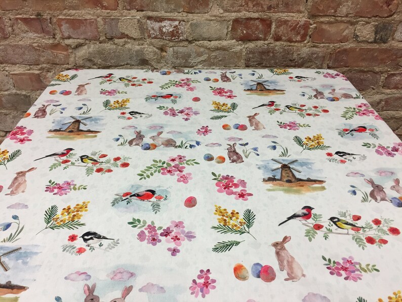 May include: White tablecloth with a repeating pattern of colorful birds, bunnies, flowers, and windmills. The pattern is on a white background with a subtle texture.