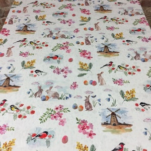 May include: White tablecloth with a repeating pattern of colorful Easter eggs, bunnies, birds, and windmills. The pattern is on a white background with a subtle texture.