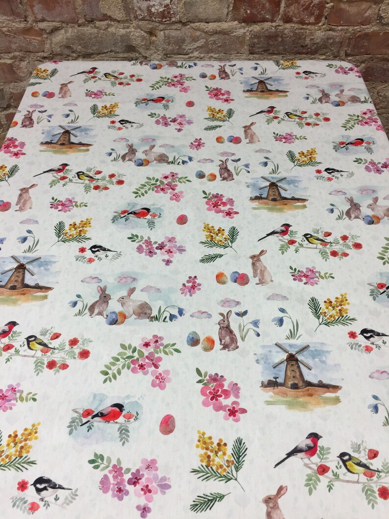 May include: White tablecloth with a repeating pattern of colorful Easter eggs, bunnies, birds, and windmills. The pattern is on a white background with a subtle texture.