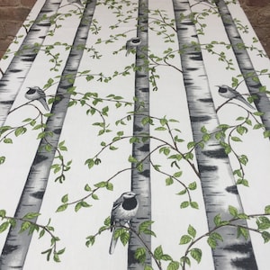 May include: White fabric with a repeating pattern of birch trees and small black and white birds. The trees have a gray bark with black markings and green leaves.