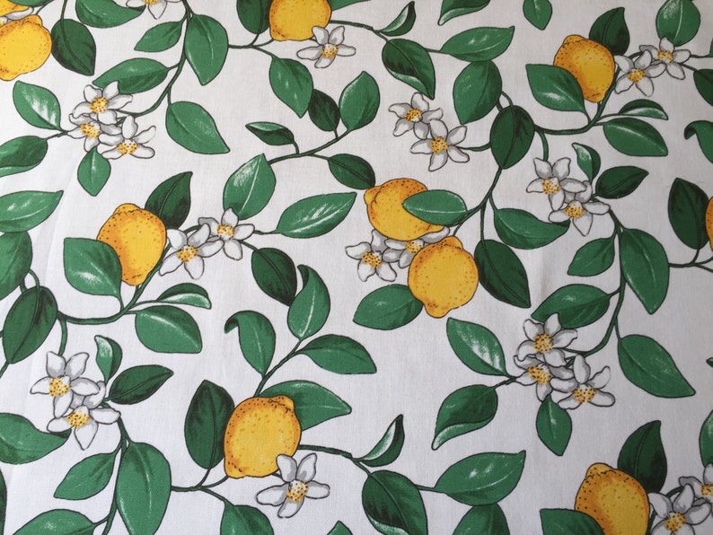 May include: White fabric with a repeating pattern of green leaves, white blossoms, and yellow lemons.