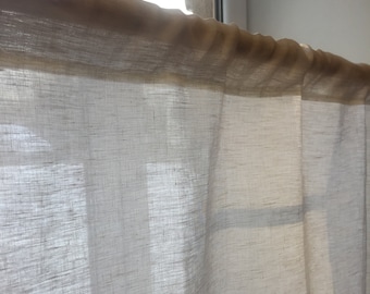 May include: A sheer white linen curtain with a beige top hem. The curtain is hanging in a window and is letting in natural light.