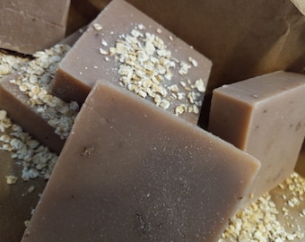 May include: Close-up of several brown, rectangular bars of soap. Some bars are topped with scattered oatmeal flakes. The soap has a natural, handmade appearance, suggesting a focus on organic ingredients and skincare.