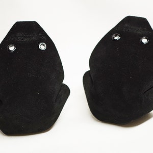 May include: Two black suede shoe protectors with eyelets. The protectors are shaped like a shoe toe and are designed to protect the front of shoes from scuffs and scratches.