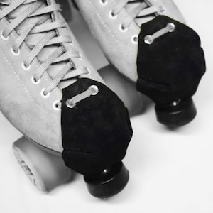 May include: A pair of white roller skates with black toe guards. The skates have laces and are tied. The wheels are black.