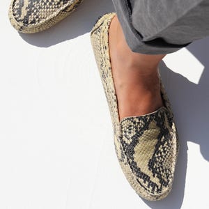 Peut inclure: Mocassins à motif peau de serpent beige et noir. Les chaussures ont un bout arrondi et un profil bas. Portées avec un pantalon gris.
