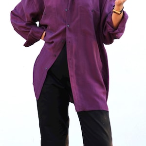 May include: A long-sleeved, button-down shirt in a deep purple hue. The shirt features a classic collar, buttoned cuffs, and two chest pockets. Paired with black pants, the outfit presents a relaxed, yet stylish aesthetic.
