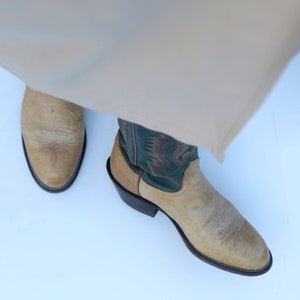 May include: A pair of tan cowboy boots with green embroidered details. The boots have a pointed toe and a low heel.