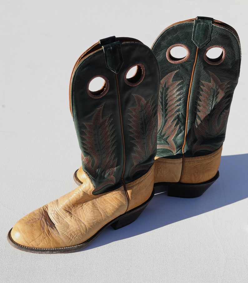 May include: A pair of tan leather cowboy boots with green leather tops and decorative stitching. The boots have a pointed toe and a stacked heel.