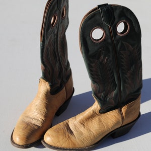 May include: A pair of tan cowboy boots with green leather tops. The boots have a pointed toe and a decorative stitching pattern.