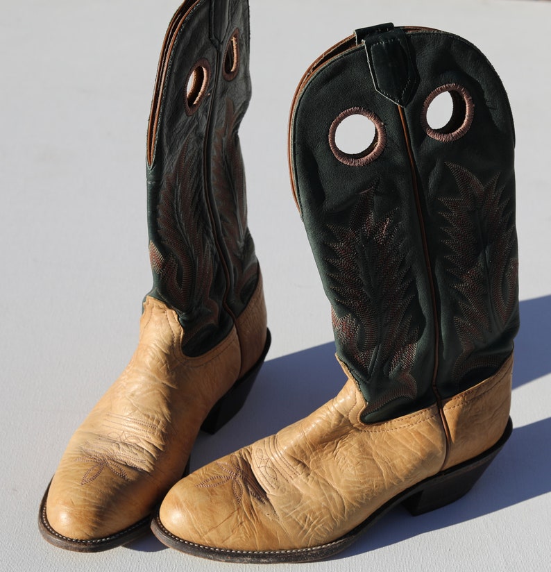 May include: A pair of tan cowboy boots with green leather tops. The boots have a pointed toe and a decorative stitching pattern.