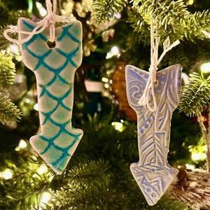 May include: Two ceramic arrow ornaments with a white background and blue designs. One arrow has a blue and white geometric pattern, and the other has a blue and white floral pattern.