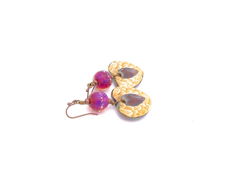 Earrings made with a heart-shaped charm featuring 2 angel wings in shades of cream with maroon in the center hang below matching maroon handmade lampwork glass beads.  Hand wrapped with copper wire.  Copper ear wires.