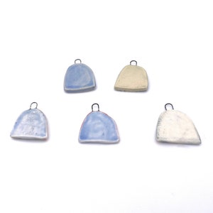 Five ceramic pendants with metal loops. Two pendants are light blue, two are white, and one is a light beige color. The pendants are all in the shape of a rounded rectangle.