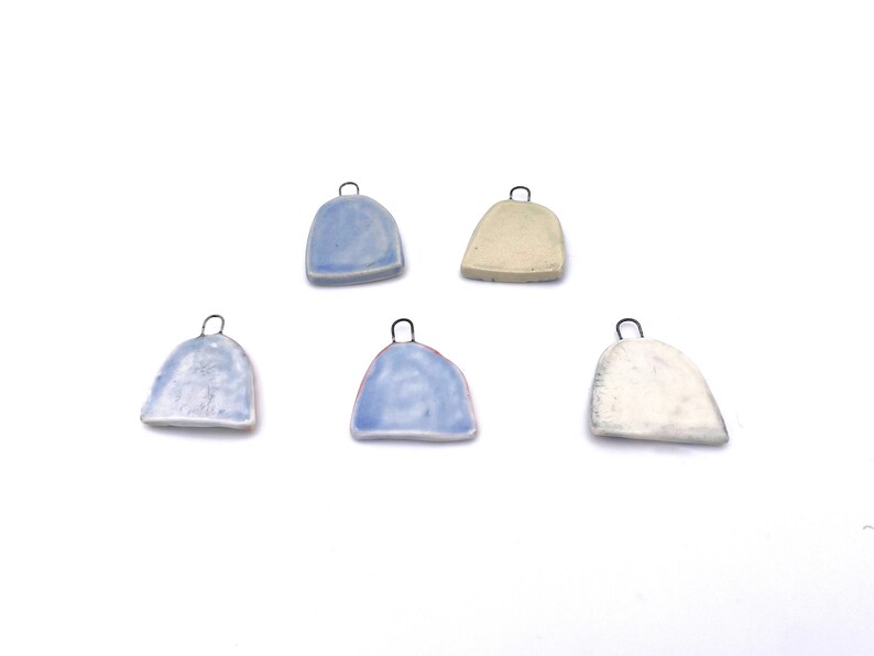 Five ceramic pendants with metal loops. Two pendants are light blue, two are white, and one is a light beige color. The pendants are all in the shape of a rounded rectangle.