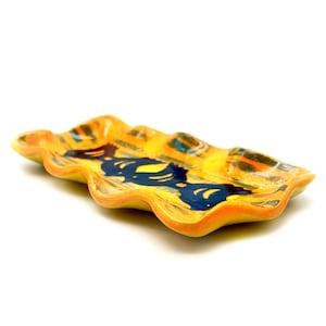 May include: A yellow ceramic serving dish with a wavy edge and a blue and yellow patterned design. The dish is perfect for serving snacks or appetizers.