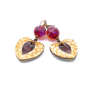 Earrings made with a heart-shaped charm featuring 2 angel wings in shades of cream with maroon in the center hang below matching maroon handmade lampwork glass beads.  Hand wrapped with copper wire.  Copper ear wires.