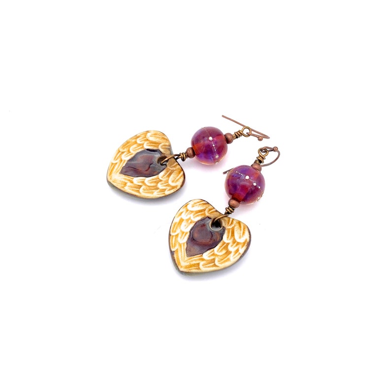 Earrings made with a heart-shaped charm featuring 2 angel wings in shades of cream with maroon in the center hang below matching maroon handmade lampwork glass beads.  Hand wrapped with copper wire.  Copper ear wires.
