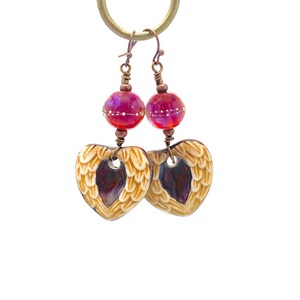 Earrings made with a heart-shaped charm featuring 2 angel wings in shades of cream with maroon in the center hang below matching maroon handmade lampwork glass beads.  Hand wrapped with copper wire.  Copper ear wires.