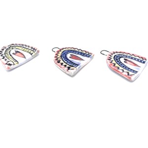 Three ceramic rainbow-shaped ornaments with a heart design in the center. The rainbows are painted in shades of blue, yellow, and red. The ornaments have a white background and a black outline.