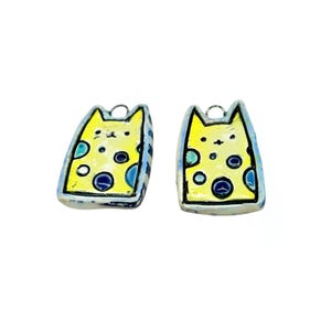 May include: Two cat-shaped earrings. Each earring features a yellow cat face with blue and green accents. The earrings have a silver-colored border and a small loop at the top for hanging. The cat's face has black dots for eyes and a nose.