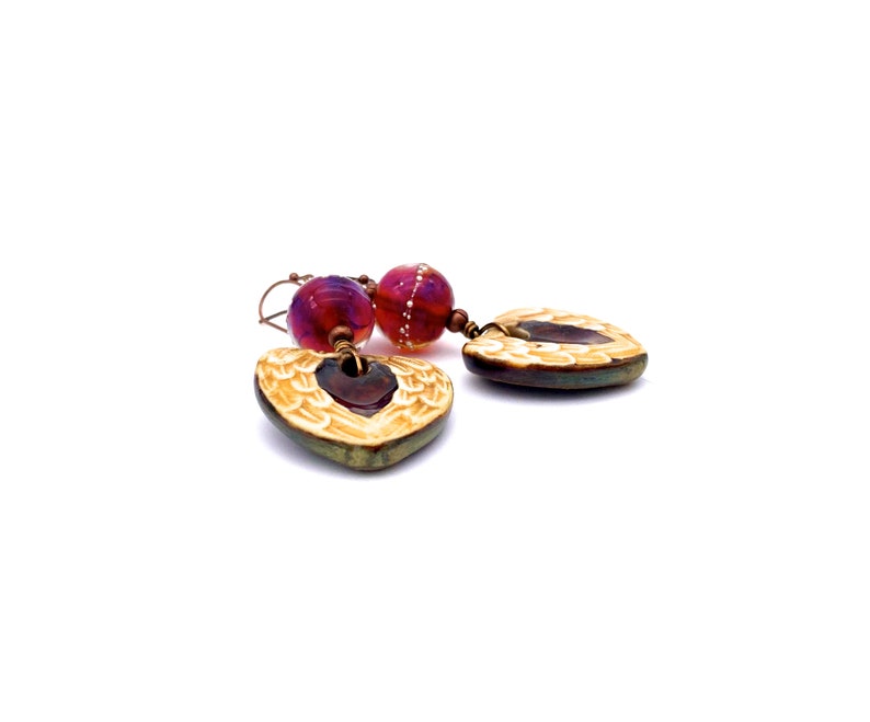 Earrings made with a heart-shaped charm featuring 2 angel wings in shades of cream with maroon in the center hang below matching maroon handmade lampwork glass beads.  Hand wrapped with copper wire.  Copper ear wires.