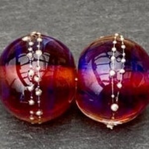 View of the 2 translucent maroon colored handmade lampwork glass beads with silver dots around the middle.