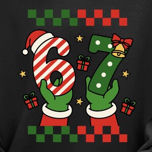 May include: Black sweatshirt with a festive Christmas design. The graphic features the numbers "6" and "7" held by green gloved hands, with a Santa hat on the "6". Presents and stars surround the numbers. The top border has a green and red pixelated pattern.