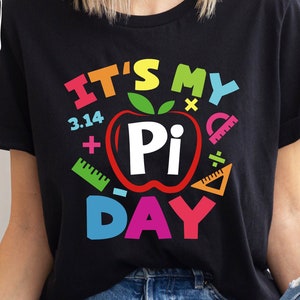 May include: Black t-shirt with a colorful graphic that says "It's My Pi Day" with a red apple with a white "Pi" inside and other colorful math symbols.
