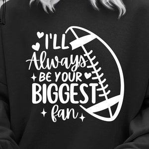 Puede incluir: Sudadera negra con texto blanco que dice "Siempre seré tu mayor fan" y un contorno blanco de un balón de fútbol.