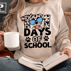 K&ouml;nnte beinhalten: Ein beiger Pullover mit einem Aufdruck eines Dalmatiners mit Sonnenbrille und dem Text "101 Days of School".