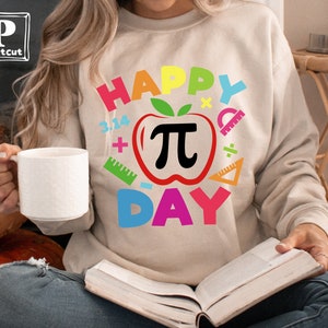 May include: A beige sweatshirt with the text "Happy Pi Day" in rainbow colors. The design includes a red apple with a black pi symbol and various math symbols.