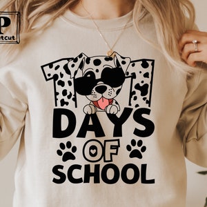 K&ouml;nnte beinhalten: Ein wei&szlig;es Sweatshirt mit einer schwarzen Grafik eines Dalmatiners mit Sonnenbrille und dem Text "101 Tage Schule".