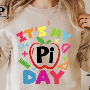 May include: A white sweatshirt with the text "It's My Pi Day" in colorful letters. The text is surrounded by various math symbols, including a red apple with a black "Pi" inside.