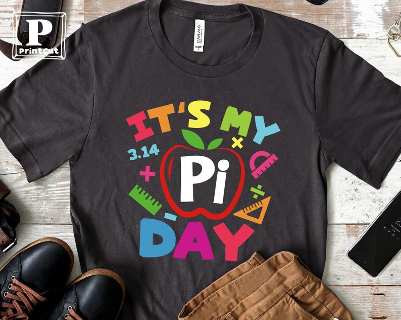 May include: A dark gray t-shirt with the text "It's My Pi Day" in colorful letters. The text is surrounded by colorful math symbols, including a red apple with a white "Pi" inside.