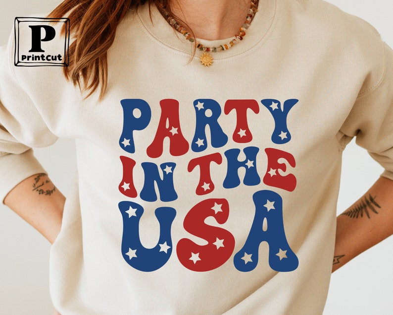 May include: A cream-colored sweatshirt with the text "Party in the USA" in red, white, and blue letters with stars.