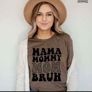 May include: A brown t-shirt with the text "Mama Mommy Mom Bruh" in black, with the word "Mom" in a leopard print pattern.
