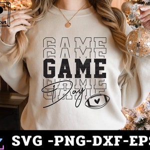 May include: A white sweatshirt with the text "GAME DAY" in black lettering. The text is stacked and repeated multiple times. A small football with a heart is below the text.
