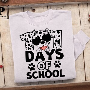 K&ouml;nnte beinhalten: Wei&szlig;es Sweatshirt mit einem schwarz-wei&szlig;en Dalmatiner, der eine Sonnenbrille und ein rotes Herz tr&auml;gt. Der Hund schaut hinter der Zahl "101" und dem Text "Days of School" hervor.