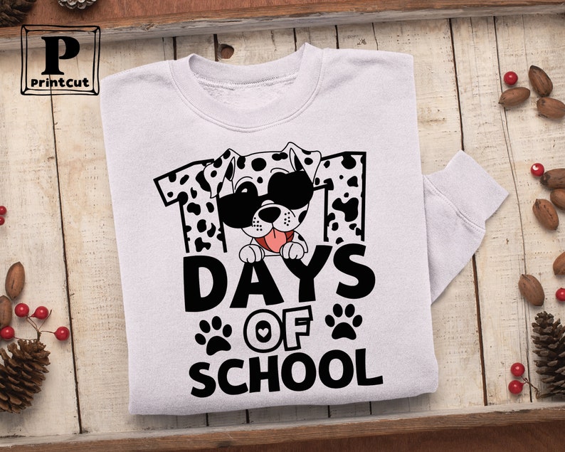 K&ouml;nnte beinhalten: Wei&szlig;es Sweatshirt mit einem schwarz-wei&szlig;en Dalmatiner, der eine Sonnenbrille und ein rotes Herz tr&auml;gt. Der Hund schaut hinter der Zahl "101" und dem Text "Days of School" hervor.
