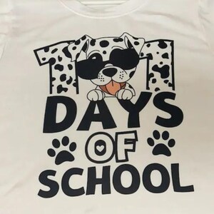 K&ouml;nnte beinhalten: Wei&szlig;es T-Shirt mit einem schwarz-wei&szlig;en Dalmatiner, der eine Sonnenbrille tr&auml;gt und den Text "101 Tage Schule" mit Pfotenabdr&uuml;cken.