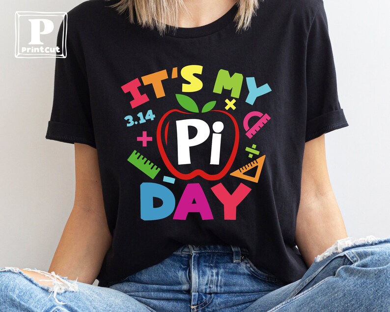 May include: Black t-shirt with a colorful graphic that says "It's My Pi Day" with a red apple with a white "Pi" inside and other colorful math symbols.