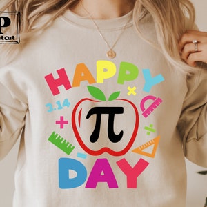 May include: A white sweatshirt with a colorful graphic design that says "Happy Pi Day". The design features a red apple with a black pi symbol inside, surrounded by colorful math symbols and the numbers 3.14.