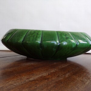 May include: A green ceramic planter with a fluted design. The planter is oval shaped and has a glossy finish.