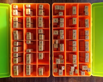 May include: An orange plastic storage case with two rows of compartments. Each compartment contains wooden letter and number stamps. The stamps are arranged alphabetically and numerically.