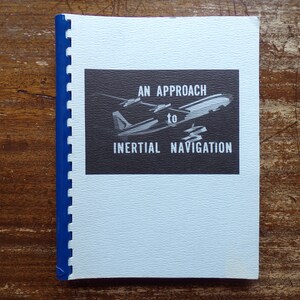 May include: A blue and white booklet with a black and white illustration of airplanes on the cover. The text on the cover reads "An Approach to Inertial Navigation".