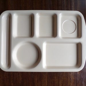 May include: A beige plastic tray with six compartments, including a round one and a rectangular one. The tray is designed for serving food.