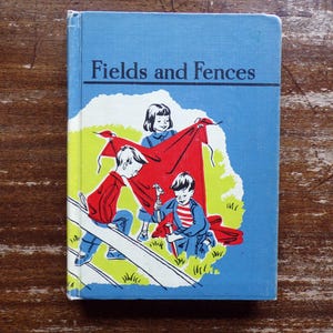 May include: Vintage children's book titled "Fields and Fences" with a blue cover. The cover illustration depicts three children playing with a red blanket near a white fence. The book's title is in black letters.