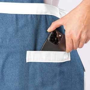 May include: A blue denim apron with a white pocket and a black smartphone in the pocket.